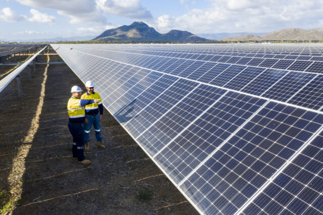 Two tradesmen standing in front of an array of solar panels with a mountain in the background.
